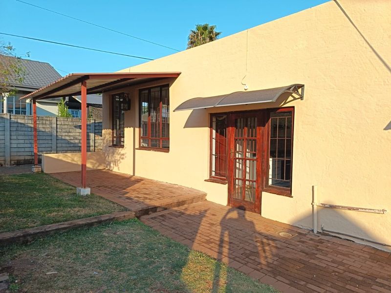 Rear exterior view of the apartment featuring a brick paved patio area, metal awning, and timber framed windows and door.