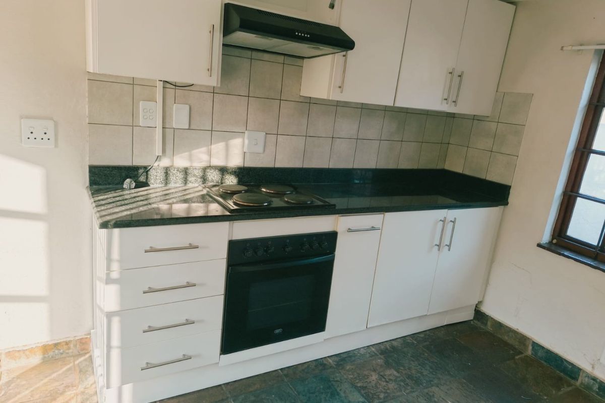 A functional kitchen featuring white cabinetry, granite countertops, a built-in oven, and an electric hob with an extractor fan.