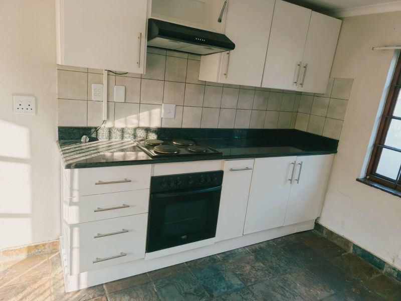 A functional kitchen featuring white cabinetry, granite countertops, a built-in oven, and an electric hob with an extractor fan.