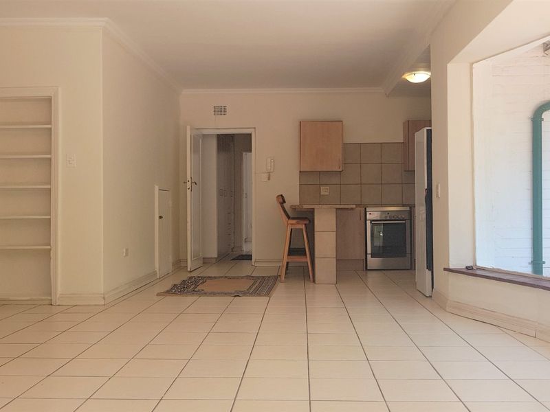 An open-plan living and kitchen area featuring tiled flooring, built-in shelving, and a functional kitchen layout with a breakfast counter.