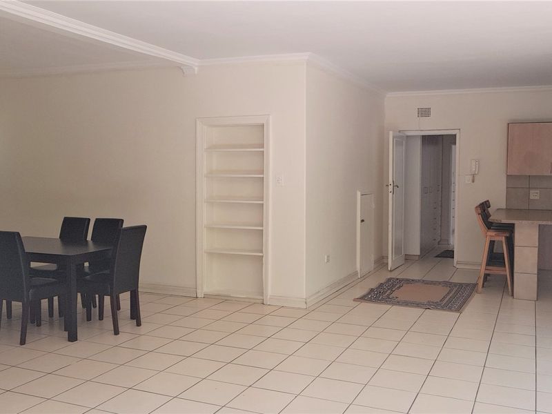 Spacious open-plan living and dining area featuring tiled floors, built-in shelving, and a functional kitchen with a breakfast bar and built-in oven.