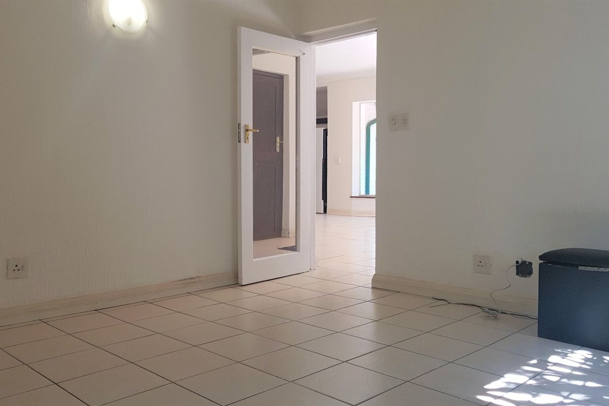 An empty living area featuring neutral tiled flooring, white walls, and a glass-panelled door leading to an adjacent room.