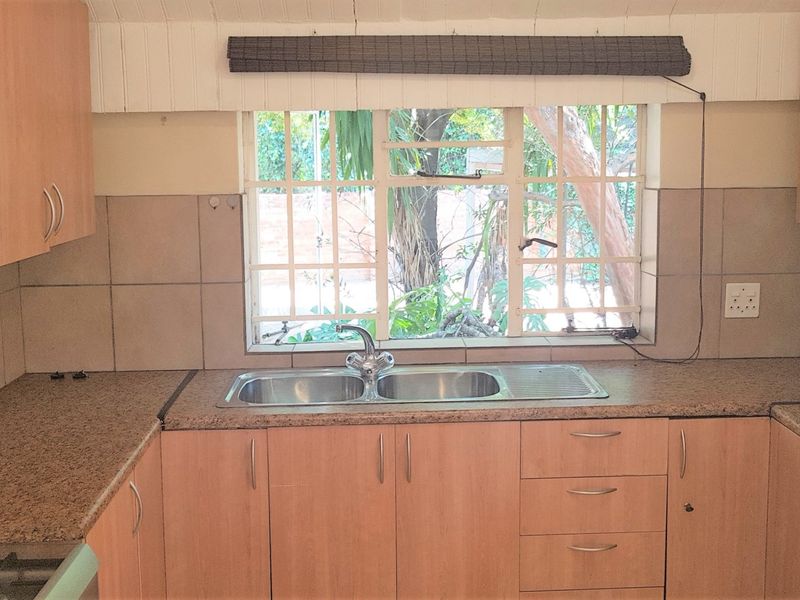 A functional kitchen featuring laminate cabinetry, granite countertops, and a double basin stainless steel sink with a view of the garden.