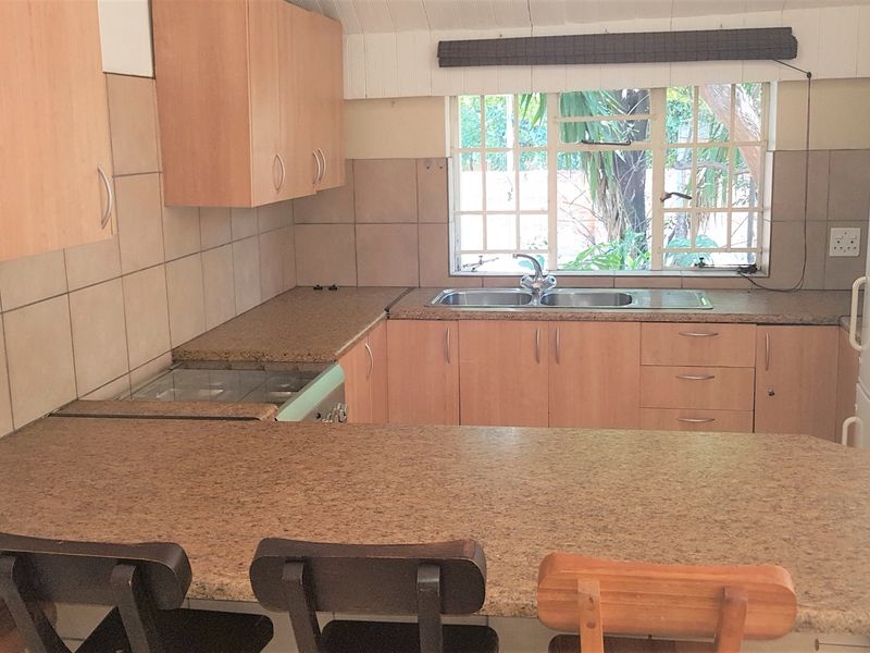 Functional kitchen featuring laminate cabinetry, granite-look countertops, a double bowl sink, and a tiled backsplash with a window overlooking the garden.