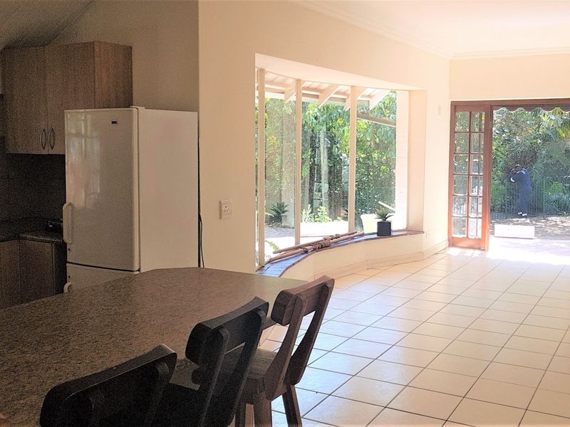 Open-plan living and kitchen area featuring tiled flooring, built-in cabinetry, and large windows with direct access to the garden through french doors.