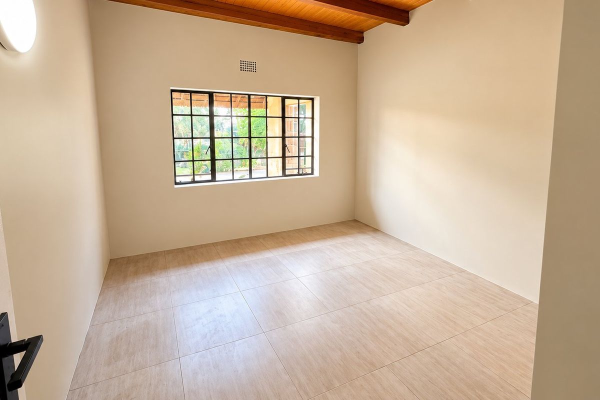 A bright, empty bedroom featuring tiled flooring, exposed timber ceiling beams, and a window with security bars.
