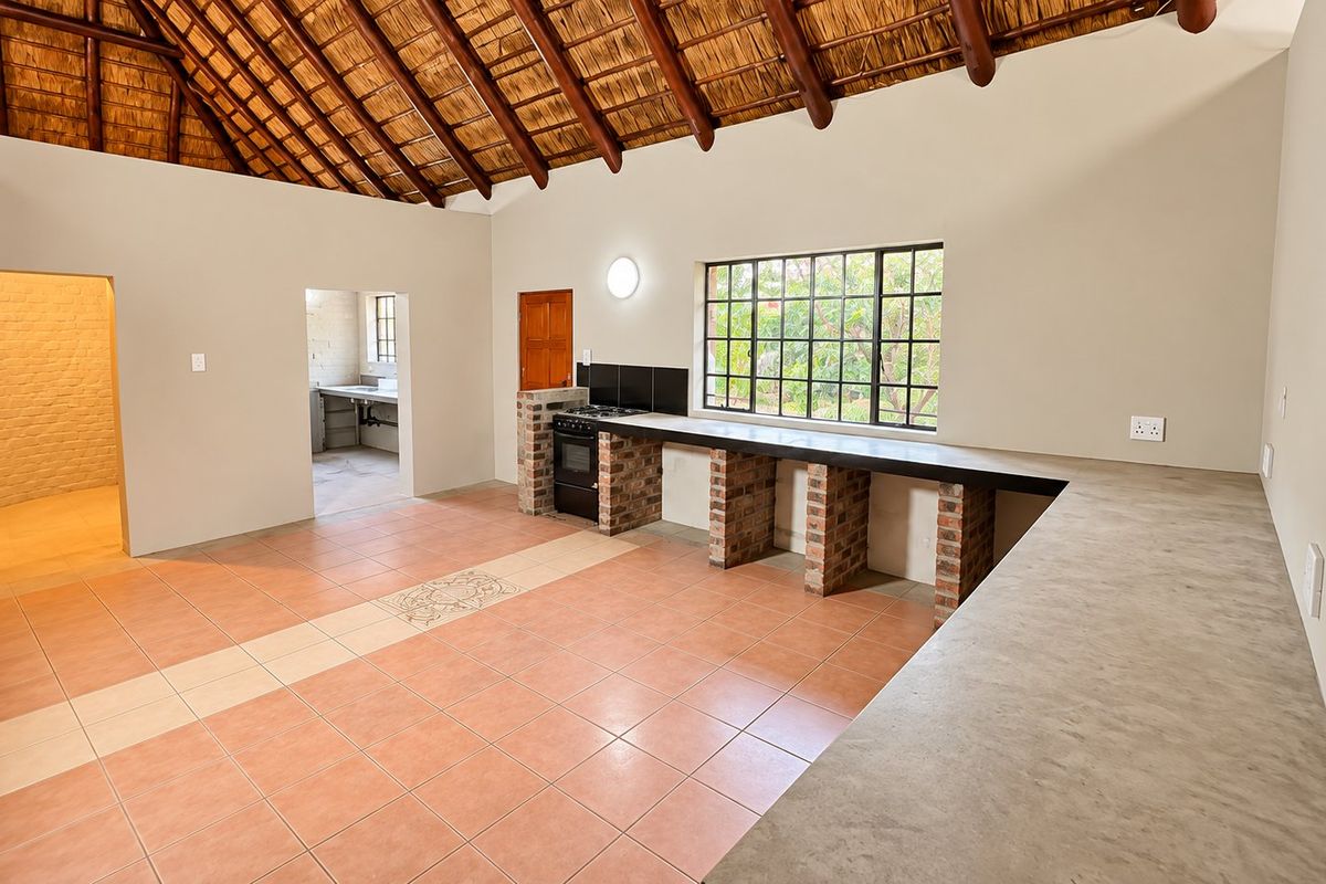 Spacious kitchen featuring a high thatched ceiling with exposed beams, concrete countertops, brick support pillars, and tiled flooring in an open-plan layout.
