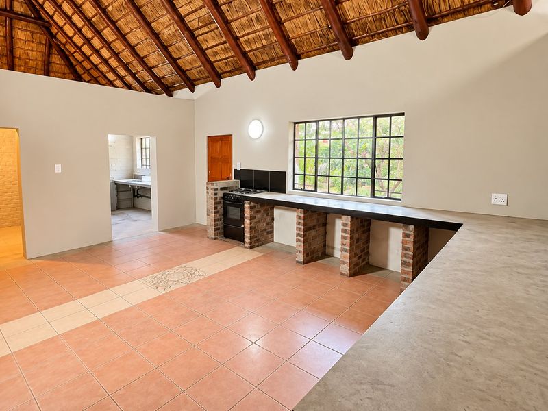 Spacious kitchen featuring a high thatched ceiling with exposed beams, concrete countertops, brick support pillars, and tiled flooring in an open-plan layout.