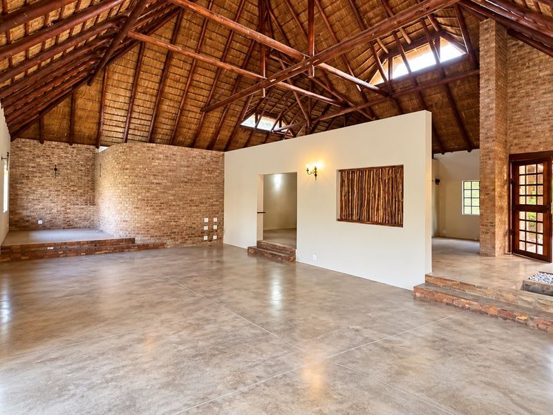 Spacious open-plan living area featuring a dramatic high-volume exposed thatch roof, timber trusses, exposed brickwork, and polished concrete floors with multi-level transitions.