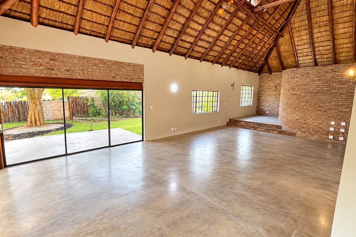 Spacious living area featuring a high thatched roof with exposed rafters, polished concrete floors, exposed brick accents, and large sliding doors opening to the garden.