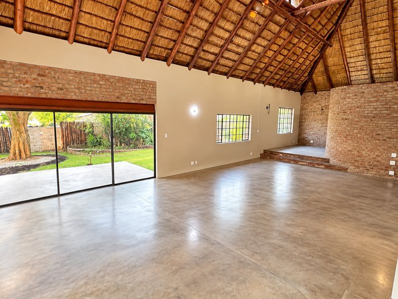 Spacious living area featuring a high thatched roof with exposed rafters, polished concrete floors, exposed brick accents, and large sliding doors opening to the garden.
