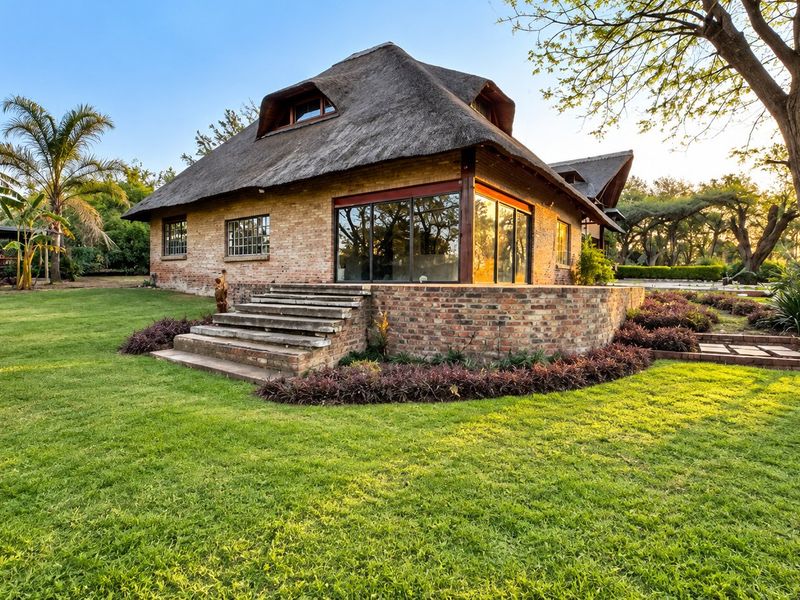 A charming rear view of a thatched-roof house featuring exposed brickwork, large glass sliding doors, and a well-maintained garden setting.
