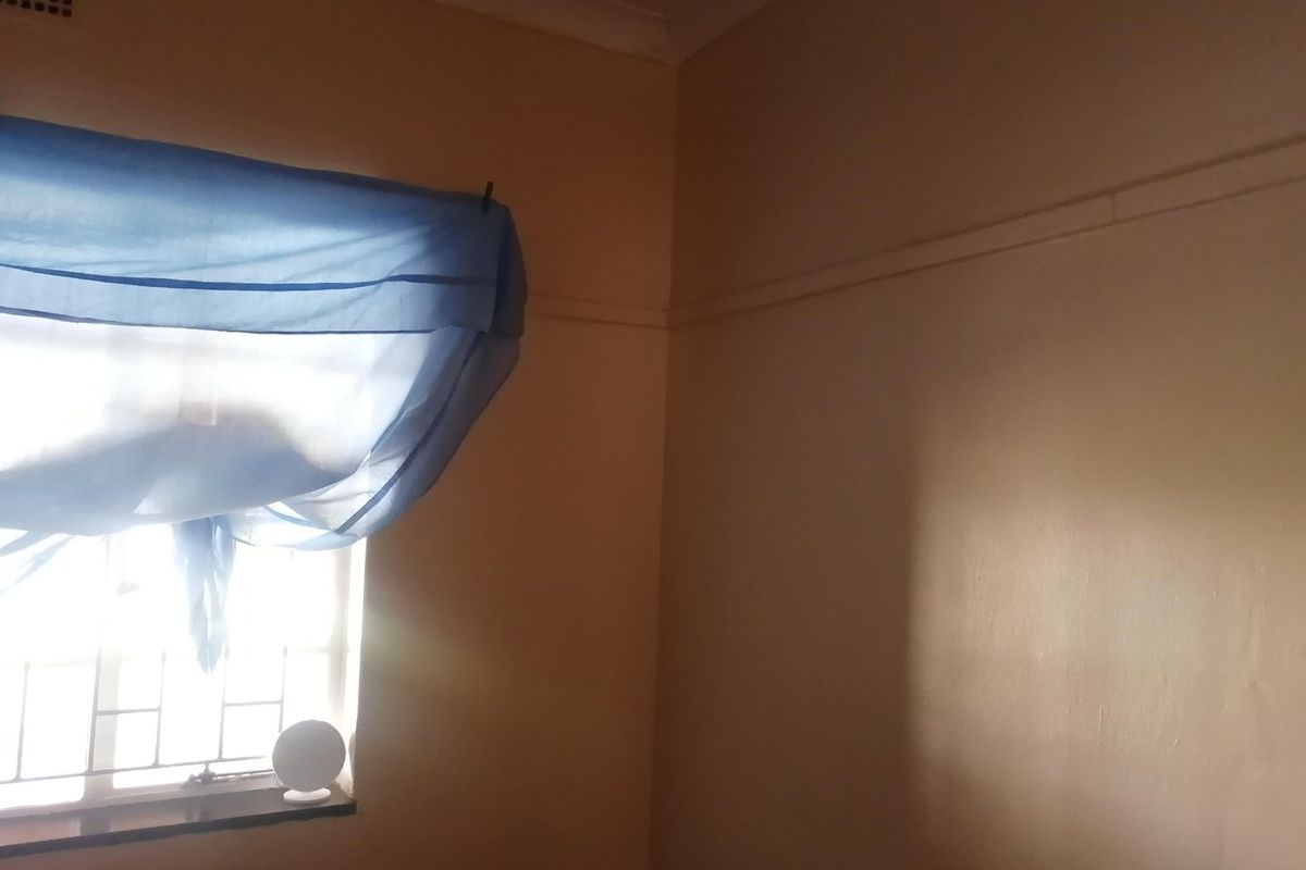A corner view of a bedroom featuring a window with security bars, picture rails, and ceiling cornicing.