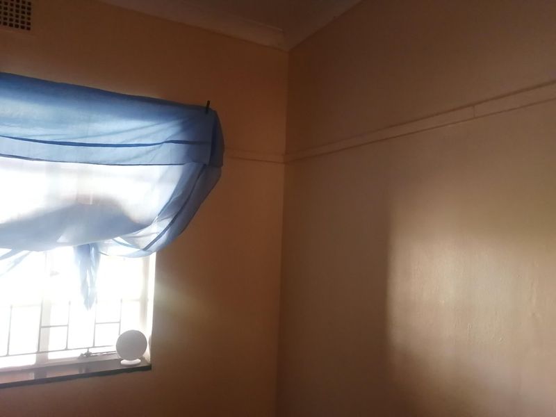 A corner view of a bedroom featuring a window with security bars, picture rails, and ceiling cornicing.
