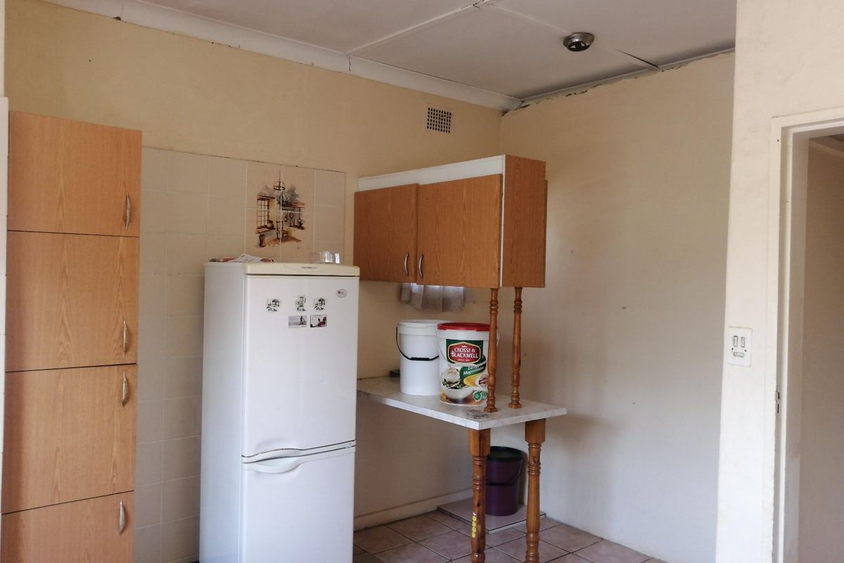 A dated kitchen area featuring built-in cabinetry, tiled flooring, and a tiled splashback, currently requiring cosmetic updates and ceiling repairs.