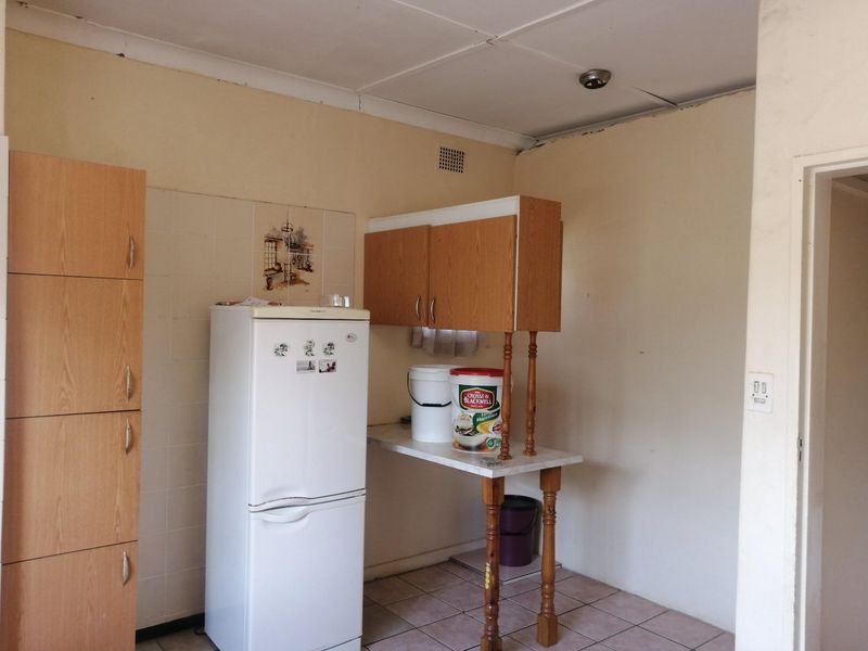 A dated kitchen area featuring built-in cabinetry, tiled flooring, and a tiled splashback, currently requiring cosmetic updates and ceiling repairs.
