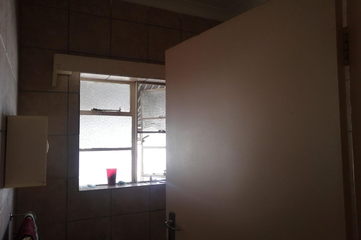 A dated bathroom featuring tiled walls, a metal frame window, and a basic basin, requiring modernization to improve its aesthetic and functionality.