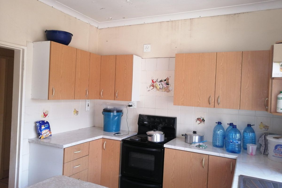 A dated kitchen featuring laminate cabinetry, tiled splashbacks, and a freestanding stove, currently showing signs of ceiling and wall surface deterioration.