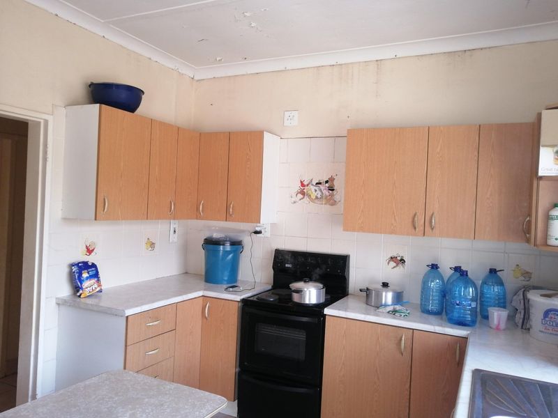 A dated kitchen featuring laminate cabinetry, tiled splashbacks, and a freestanding stove, currently showing signs of ceiling and wall surface deterioration.