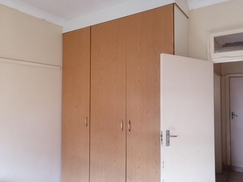 A bedroom featuring a built-in wooden wardrobe and a standard door, presenting a blank canvas for potential interior updates.