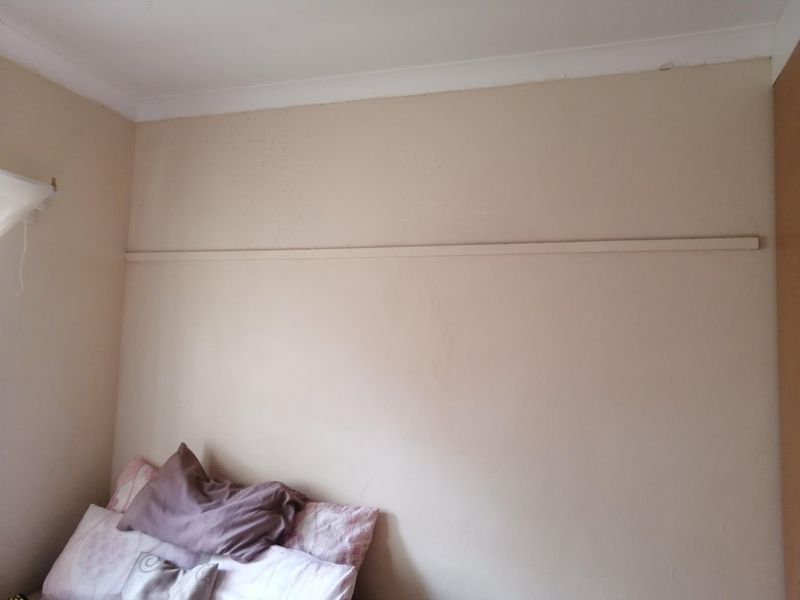 A bedroom interior featuring a wall with a traditional picture rail and coving, showing signs of wear and surface cracking.