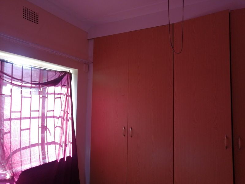 A bedroom featuring built-in wooden cupboards, a window with security bars, and a ventilation grille.