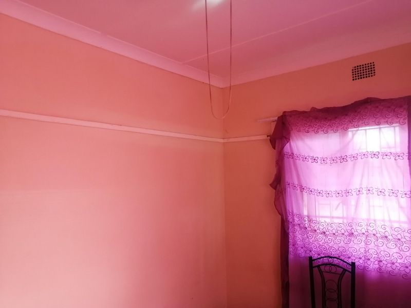 A simple, empty bedroom featuring a picture rail, coving, and a window fitted with security bars.