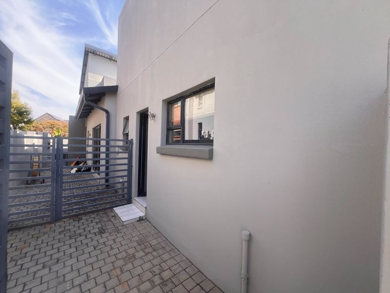 A clean rear exterior area featuring paved flooring, a secure metal gate, and modern aluminium window frames.