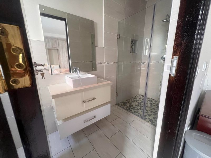 Modern bathroom featuring a floating vanity with a vessel sink, a glass-enclosed shower with a niche, and neutral wall and floor tiling.