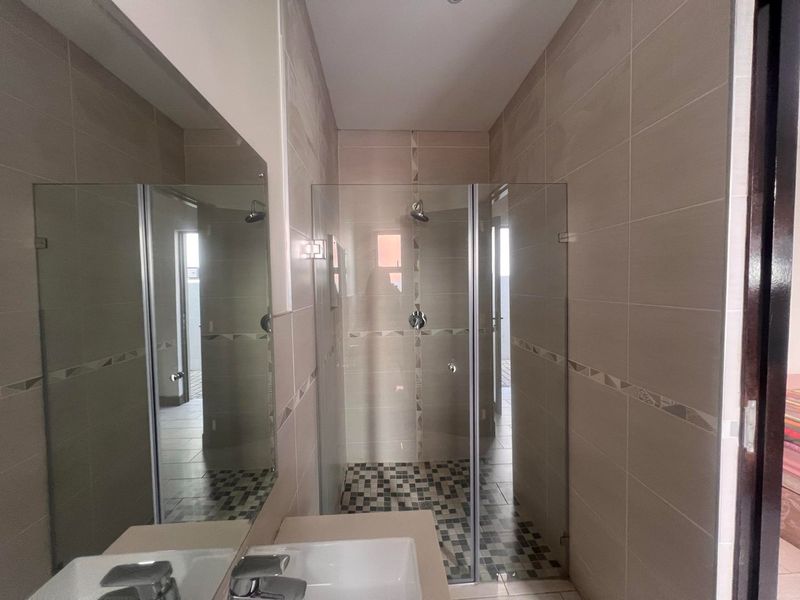 Modern bathroom featuring a walk-in shower with glass enclosure, mosaic floor tiling, vanity basin, and a large wall-mounted mirror.
