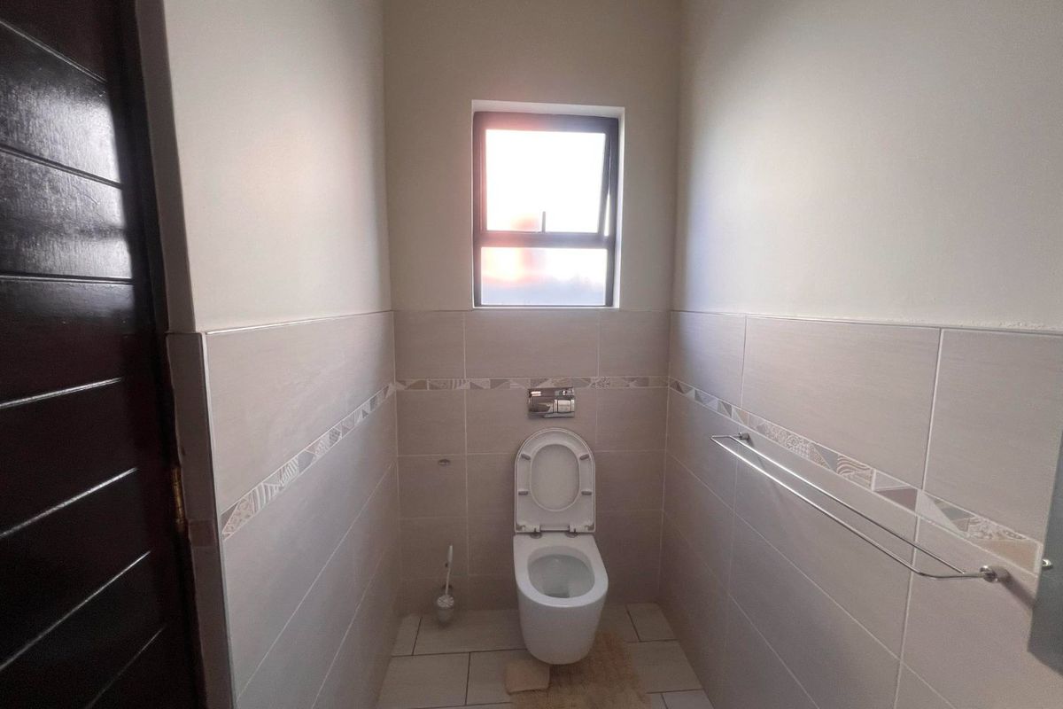 A clean and modern guest bathroom featuring neutral wall tiles, a wall-mounted toilet with a flush plate, and a functional towel rail.