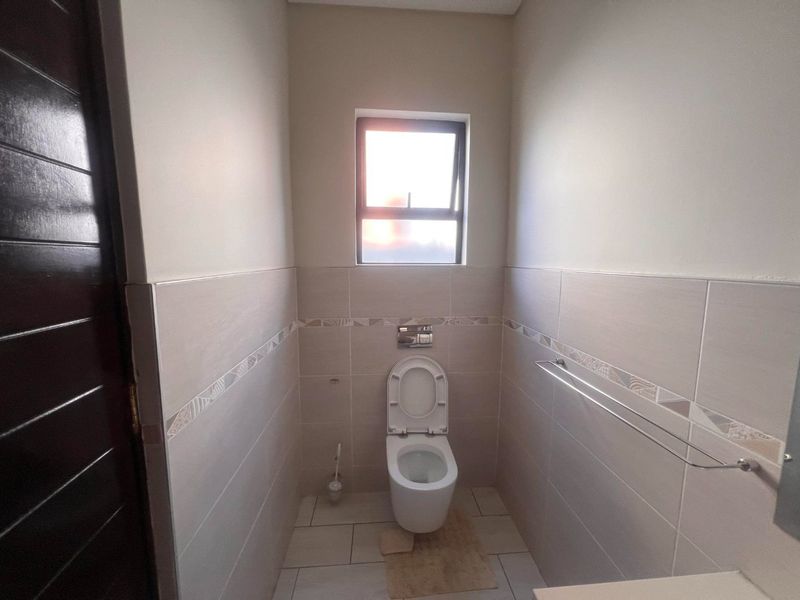 A clean and modern guest bathroom featuring neutral wall tiles, a wall-mounted toilet with a flush plate, and a functional towel rail.