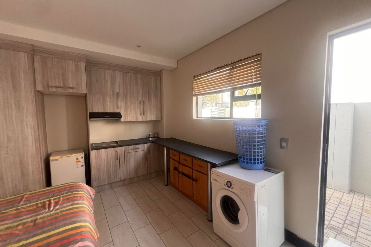 Compact kitchen area featuring wood-look cabinetry, laminate countertops, integrated hob, extractor fan, and tiled flooring with direct access to an outdoor area.