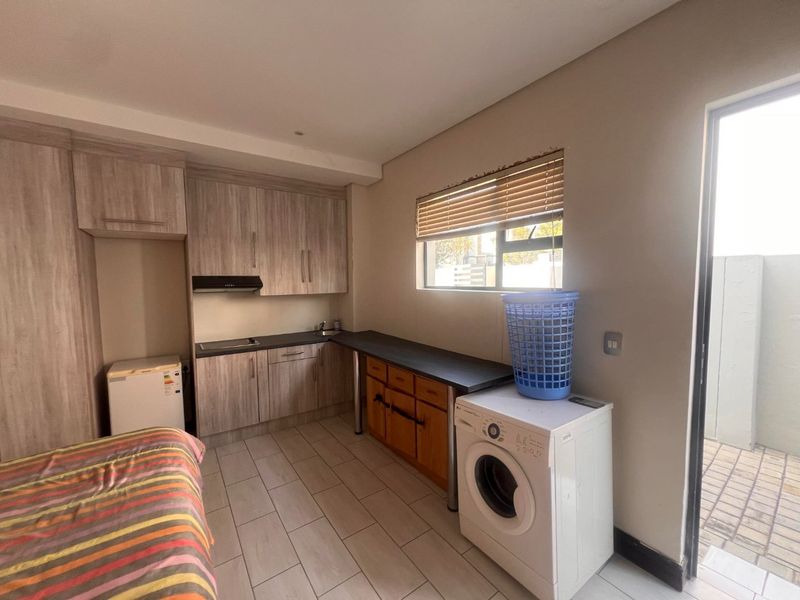 Compact kitchen area featuring wood-look cabinetry, laminate countertops, integrated hob, extractor fan, and tiled flooring with direct access to an outdoor area.