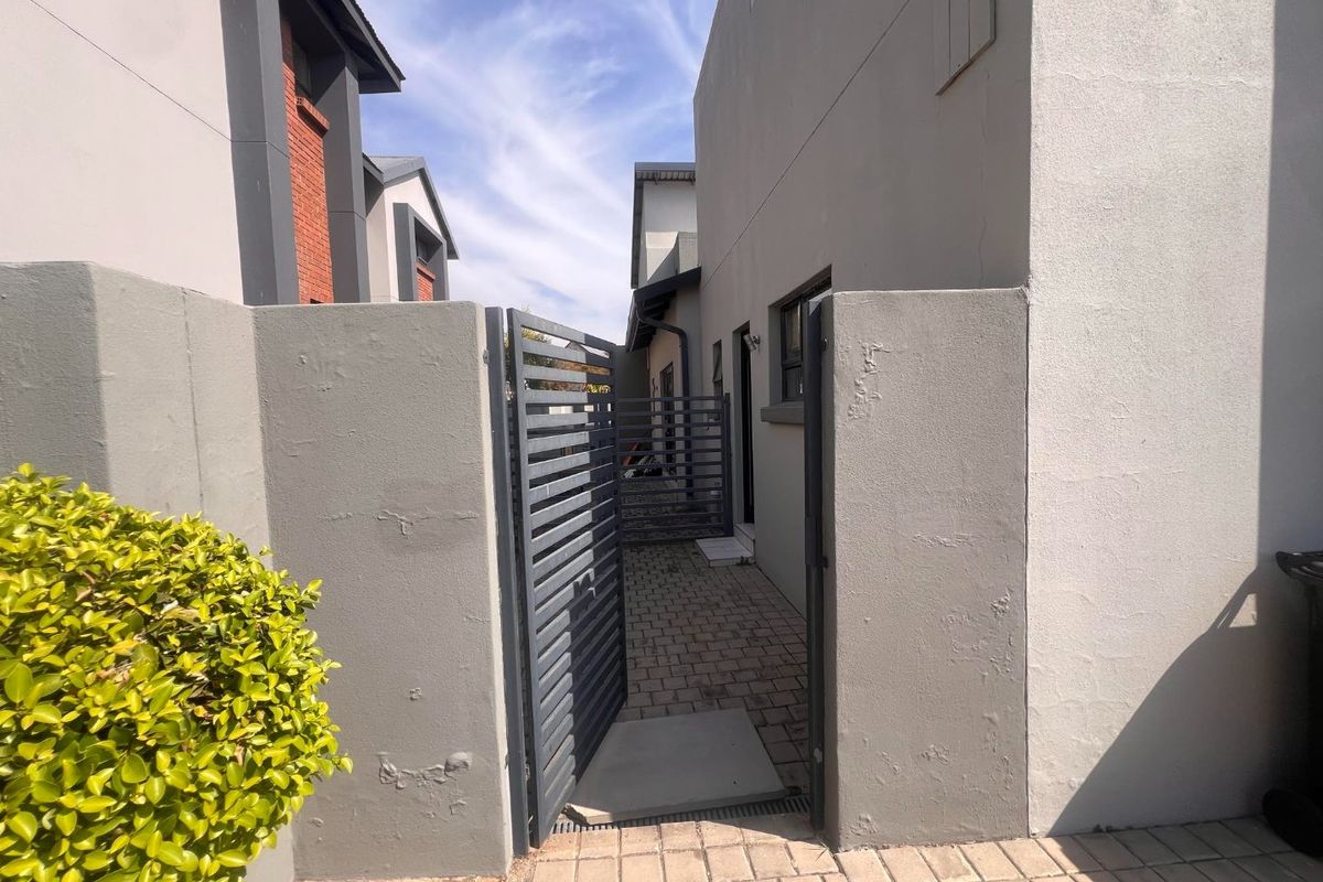 A paved side walkway leading to the rear of the property, secured by a metal gate and enclosed by plastered boundary walls.