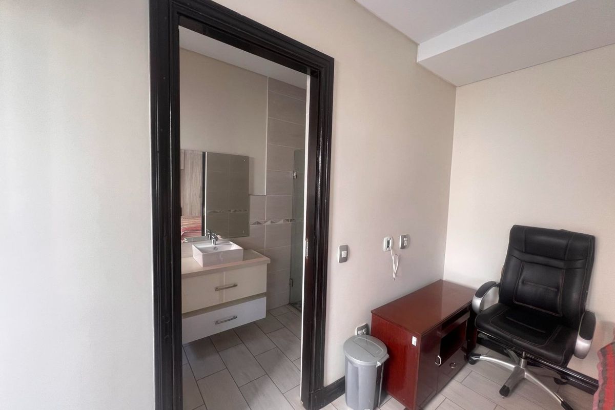 A bedroom featuring an en-suite bathroom with a modern vessel sink, vanity cabinet, and neutral tiled flooring throughout.