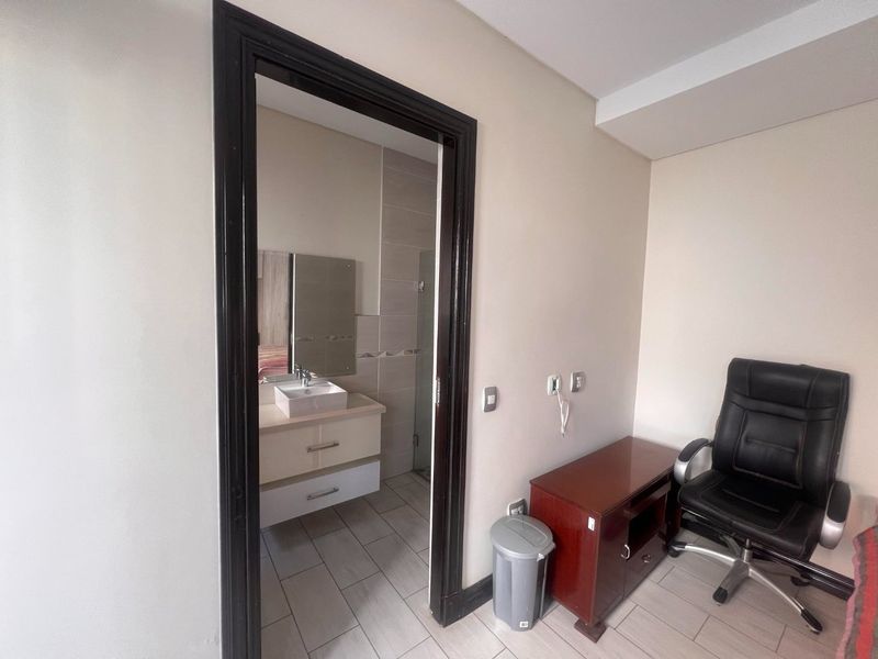 A bedroom featuring an en-suite bathroom with a modern vessel sink, vanity cabinet, and neutral tiled flooring throughout.