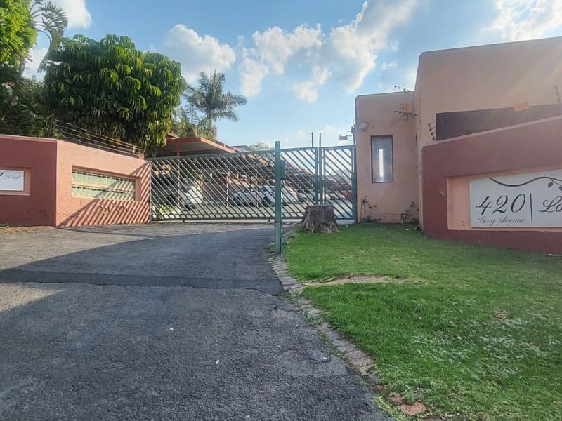 Front entrance view of Longwood complex featuring a secure gated access point, perimeter wall with electric fencing, and paved driveway.