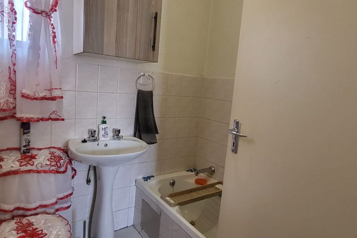 A compact bathroom featuring a pedestal basin, built-in bathtub, and wall-mounted storage cabinet with tiled splashback finishes.