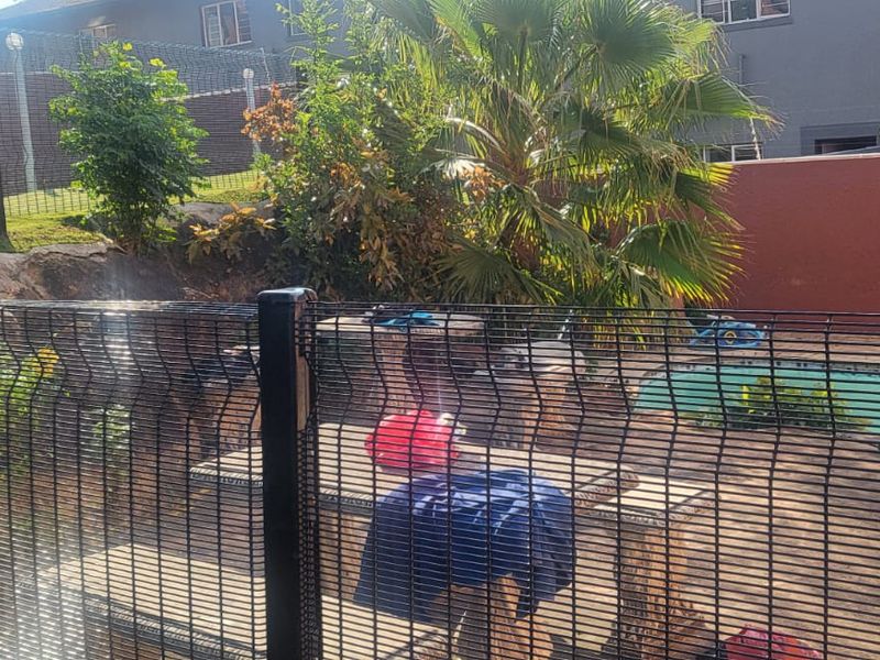 Outdoor pool area featuring a swimming pool, landscaped garden, and secure mesh perimeter fencing.