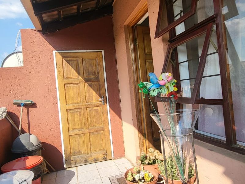 A compact balcony area featuring tiled flooring, a timber entrance door, and timber-framed top-hung windows, offering an outdoor space for the apartment.