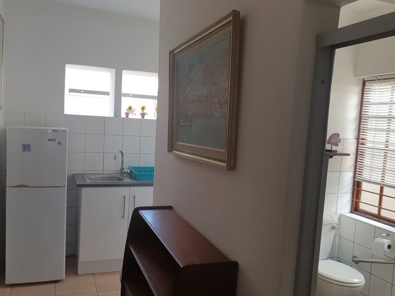 A functional scullery area featuring a stainless steel sink, tiled splashback, and built-in cabinetry, with an adjacent bathroom visible.