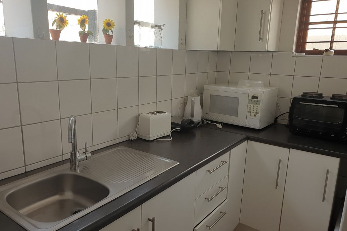 A functional kitchen featuring white cabinetry, dark laminate countertops, a stainless steel sink, and a tiled splashback.