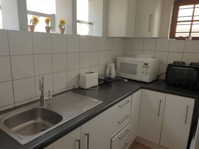 A functional kitchen featuring white cabinetry, dark laminate countertops, a stainless steel sink, and a tiled splashback.