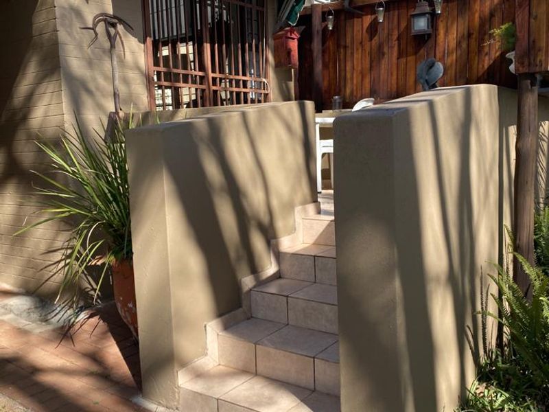 A small outdoor patio area featuring tiled steps leading to a covered entrance with a green fabric awning and secure window bars.