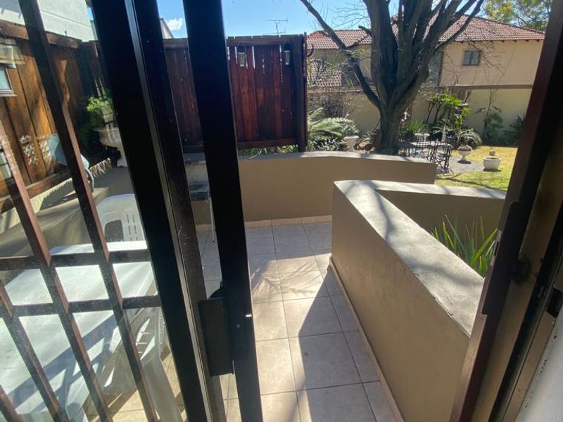 A tiled outdoor patio area featuring a built-in planter box and timber privacy screen, accessible via a sliding glass door.