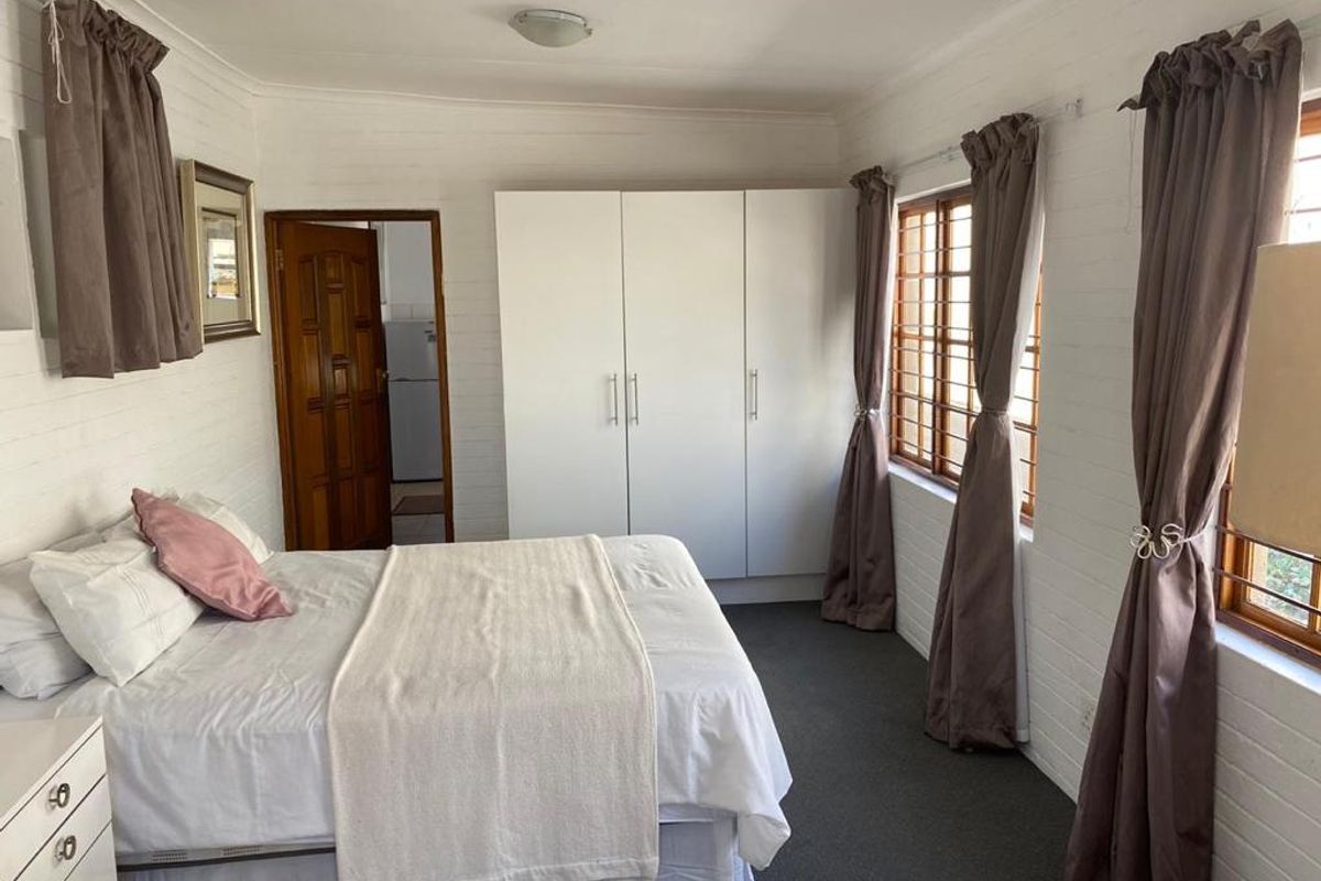 A functional bedroom featuring built-in white wardrobes, carpeted flooring, and timber-framed windows with security bars, offering a clean and practical living space.