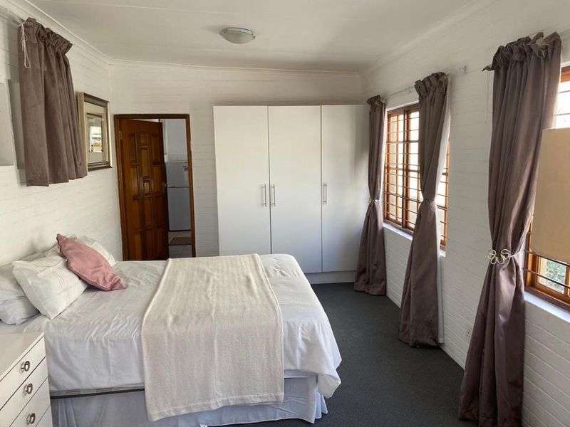 A functional bedroom featuring built-in white wardrobes, carpeted flooring, and timber-framed windows with security bars, offering a clean and practical living space.