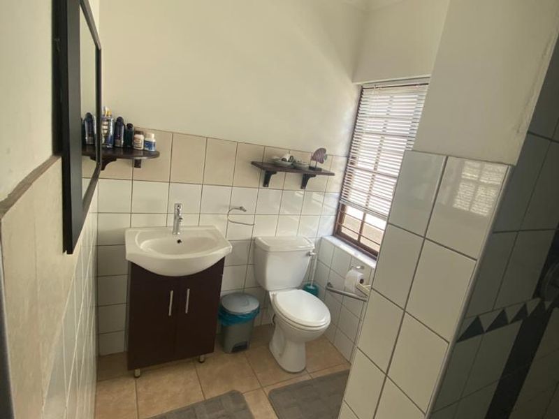 A functional bathroom featuring a vanity cabinet with basin, toilet, and neutral wall and floor tiling.