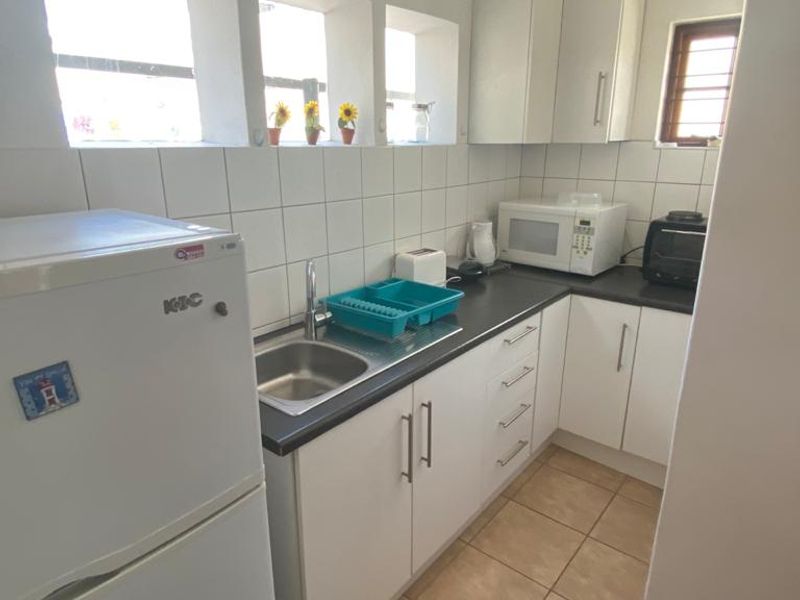 A functional kitchen featuring white cabinetry, dark laminate countertops, tiled backsplash, and ceramic floor tiles with natural light from multiple windows.